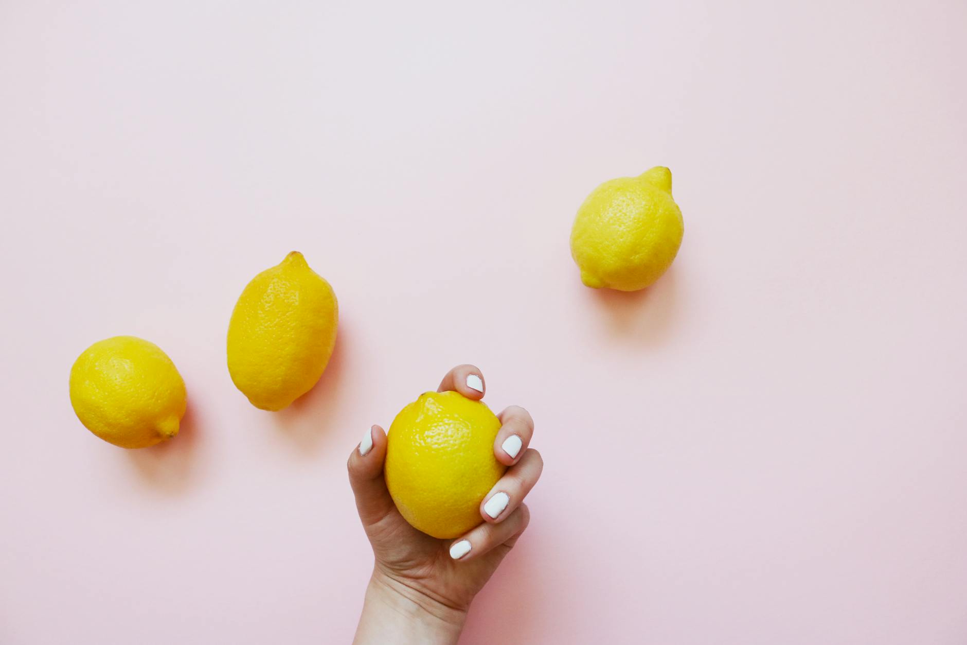 Two hands holding pink and blue silicone vibrators against a pastel background