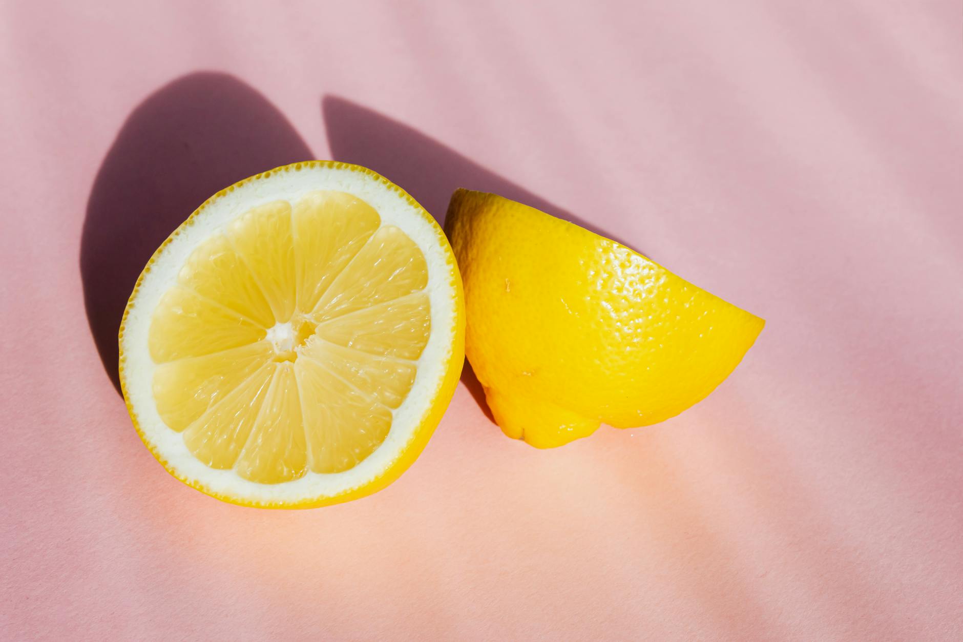 Fresh lemon halves on a pink background in sunlight, symbolizing natural pleasure and freshness