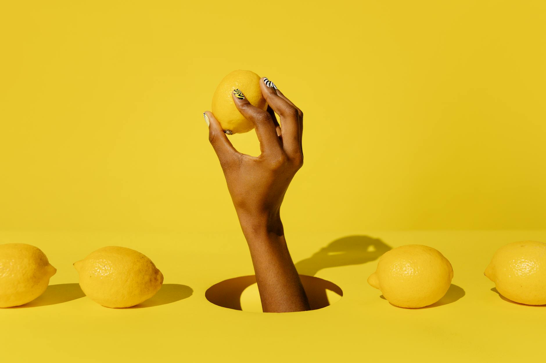 A hand holding a lemon against a bright yellow background, symbolizing fresh approaches to intimacy
