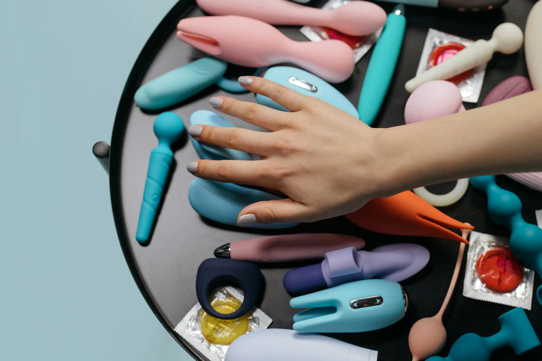 Hand reaching over a collection of colorful vibrators on a table
