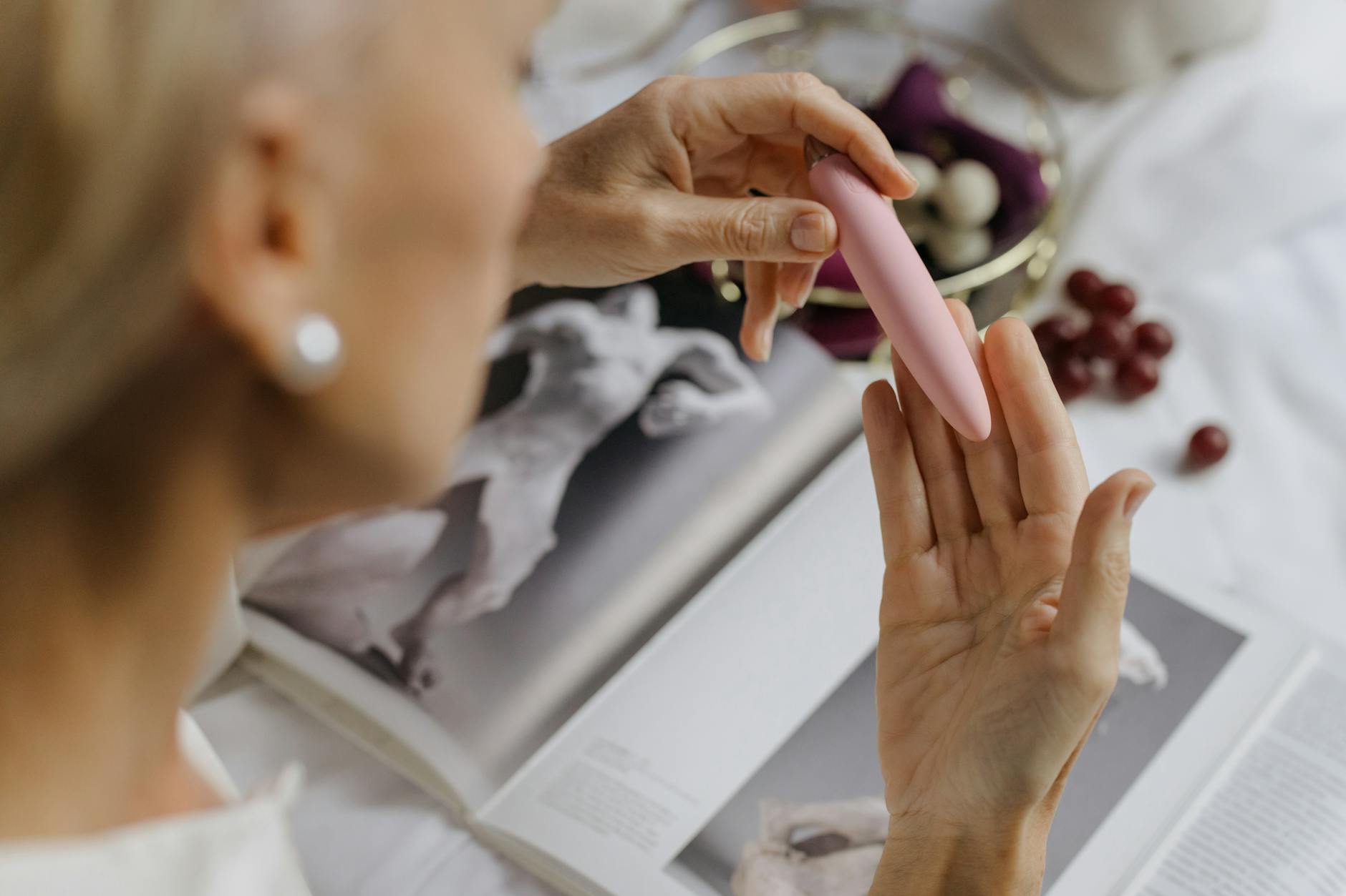Close-up of a woman holding a pink lemon clitoral vibrator against art books in soft light