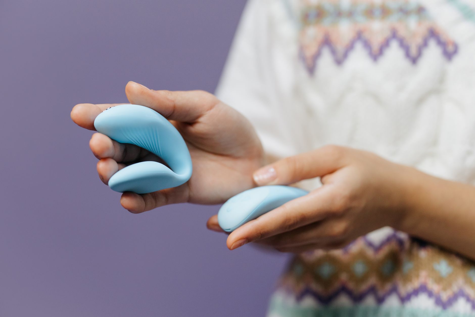 Close-up of hands holding a sleek blue vibrator against a purple background, symbolizing intimate couples pleasure.