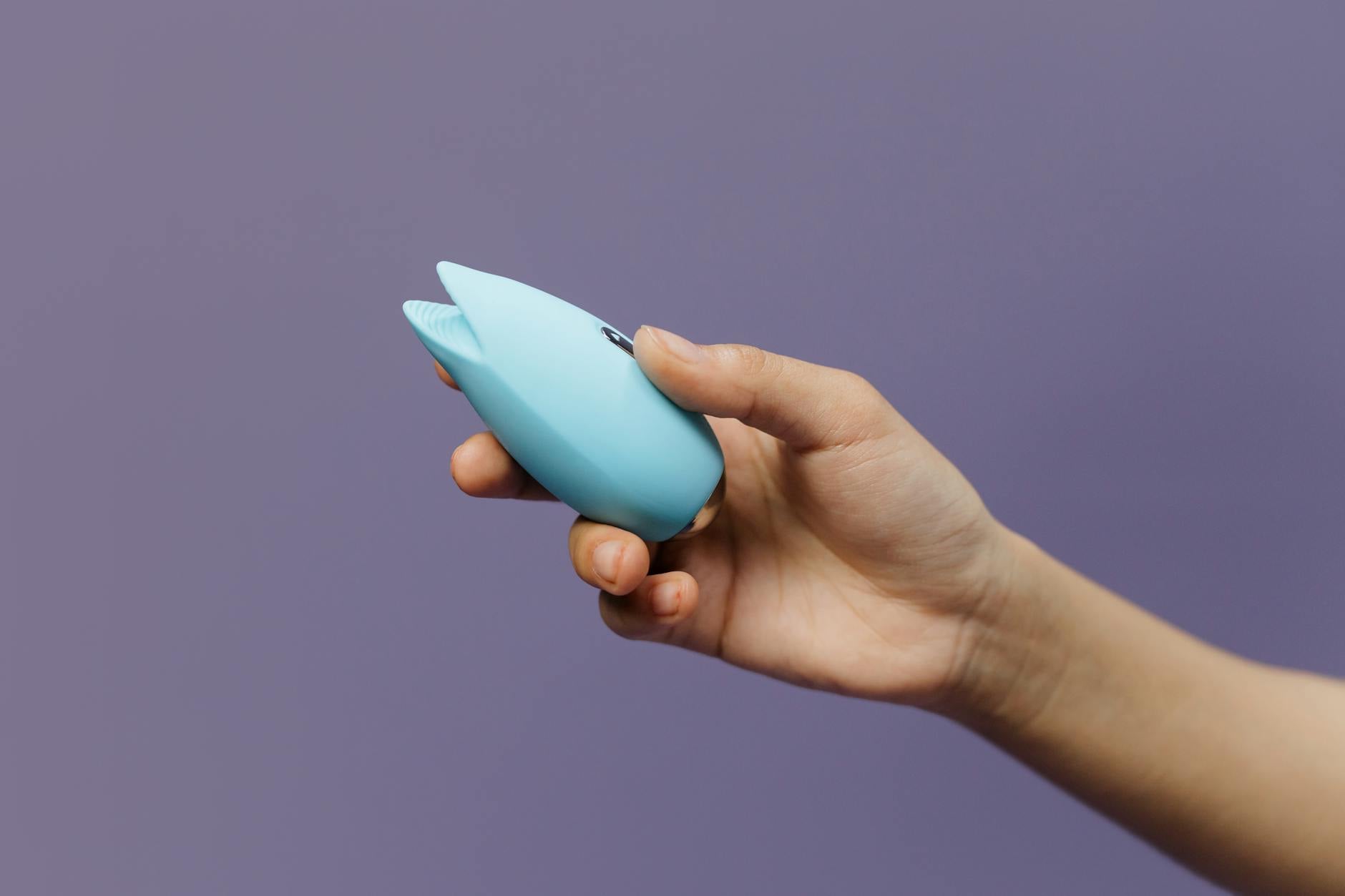 A lemon silicone vibrator held in hand against a solid purple background, promoting self-love and sexuality.