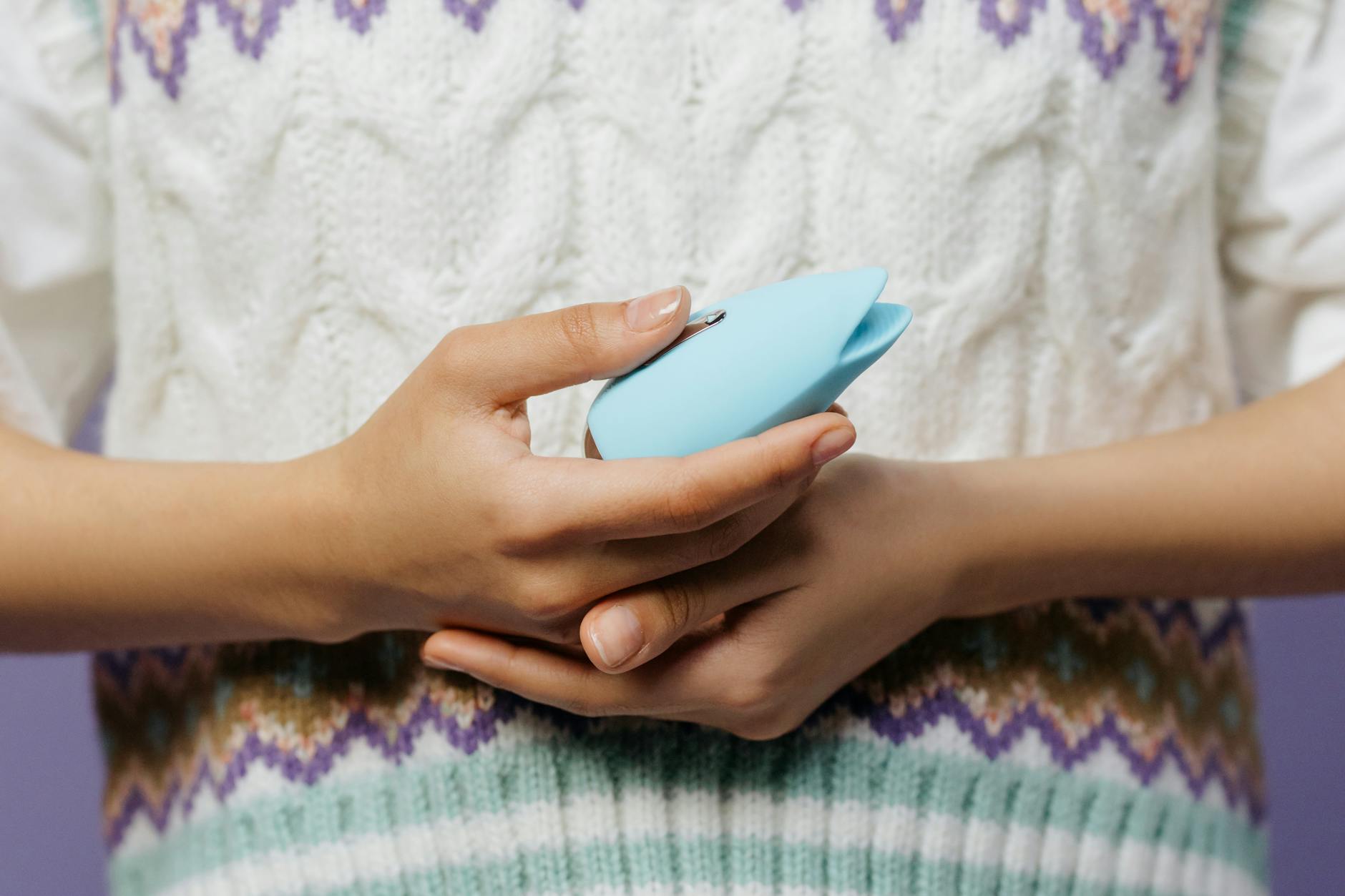 Close-up of hands holding a personal massager against a knitted sweater