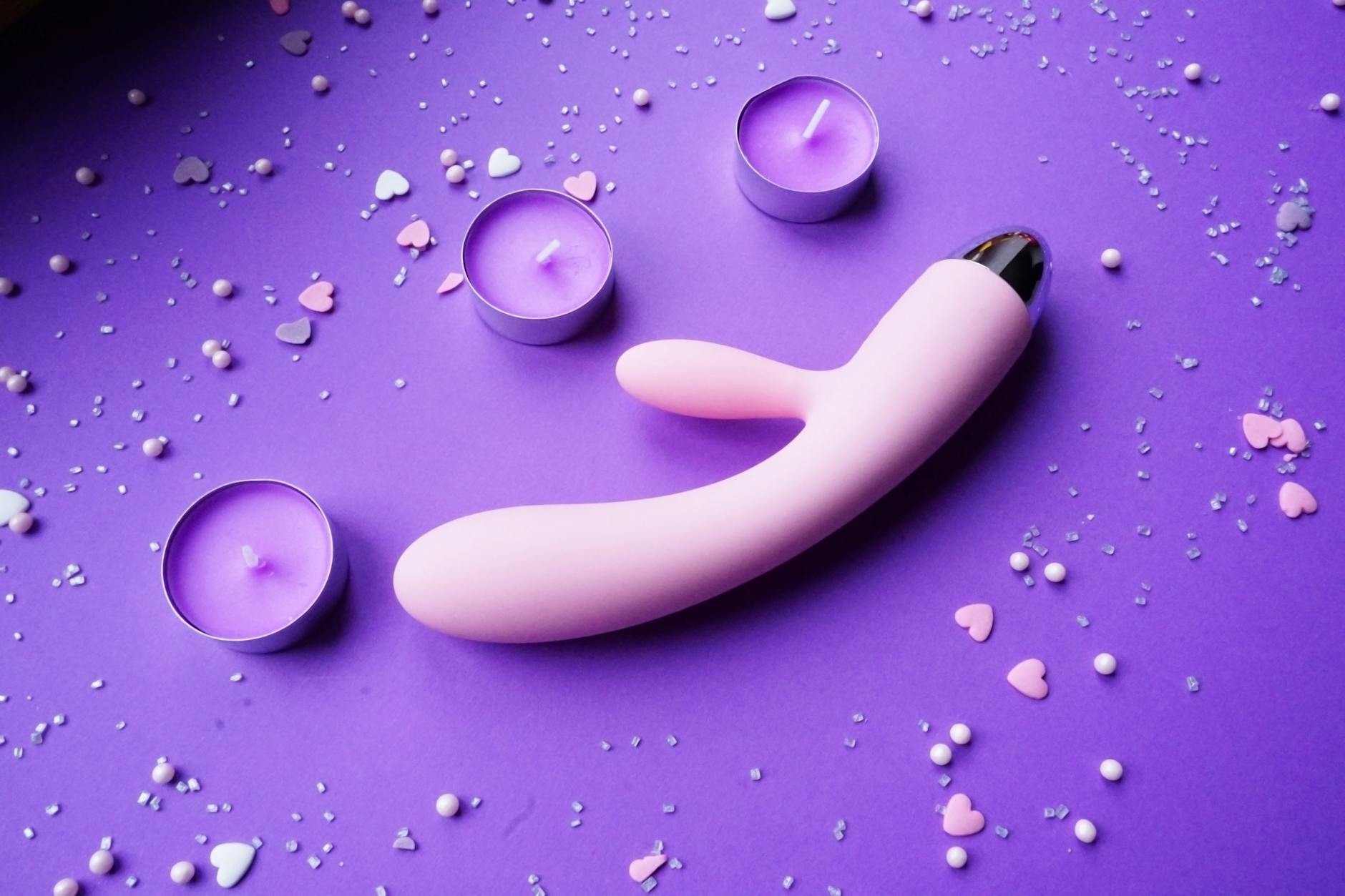 Pink vibrator on purple background with heart confetti and candles for a romantic vibe
