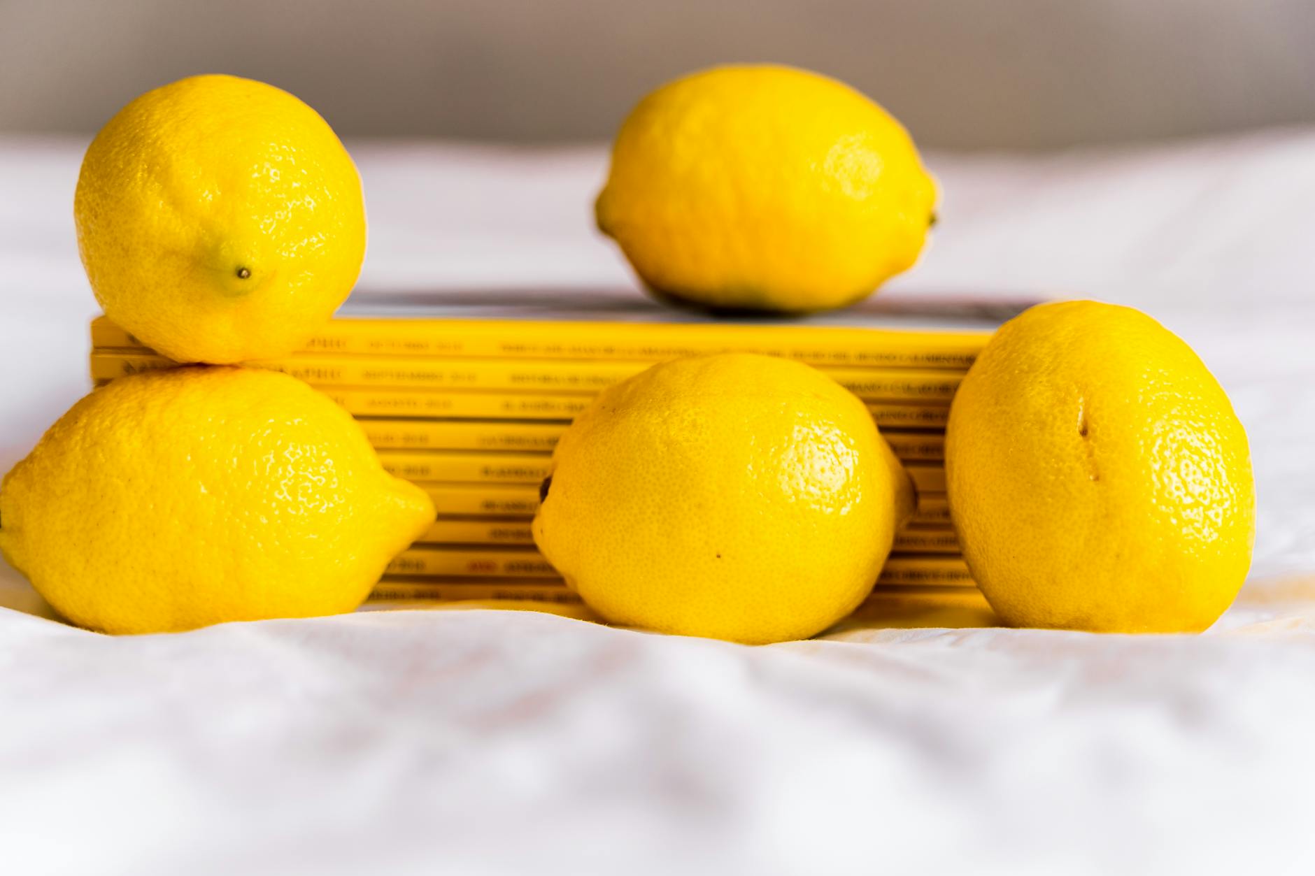 Hand holding a fresh lemon against a soft pink background with more lemons surrounding it